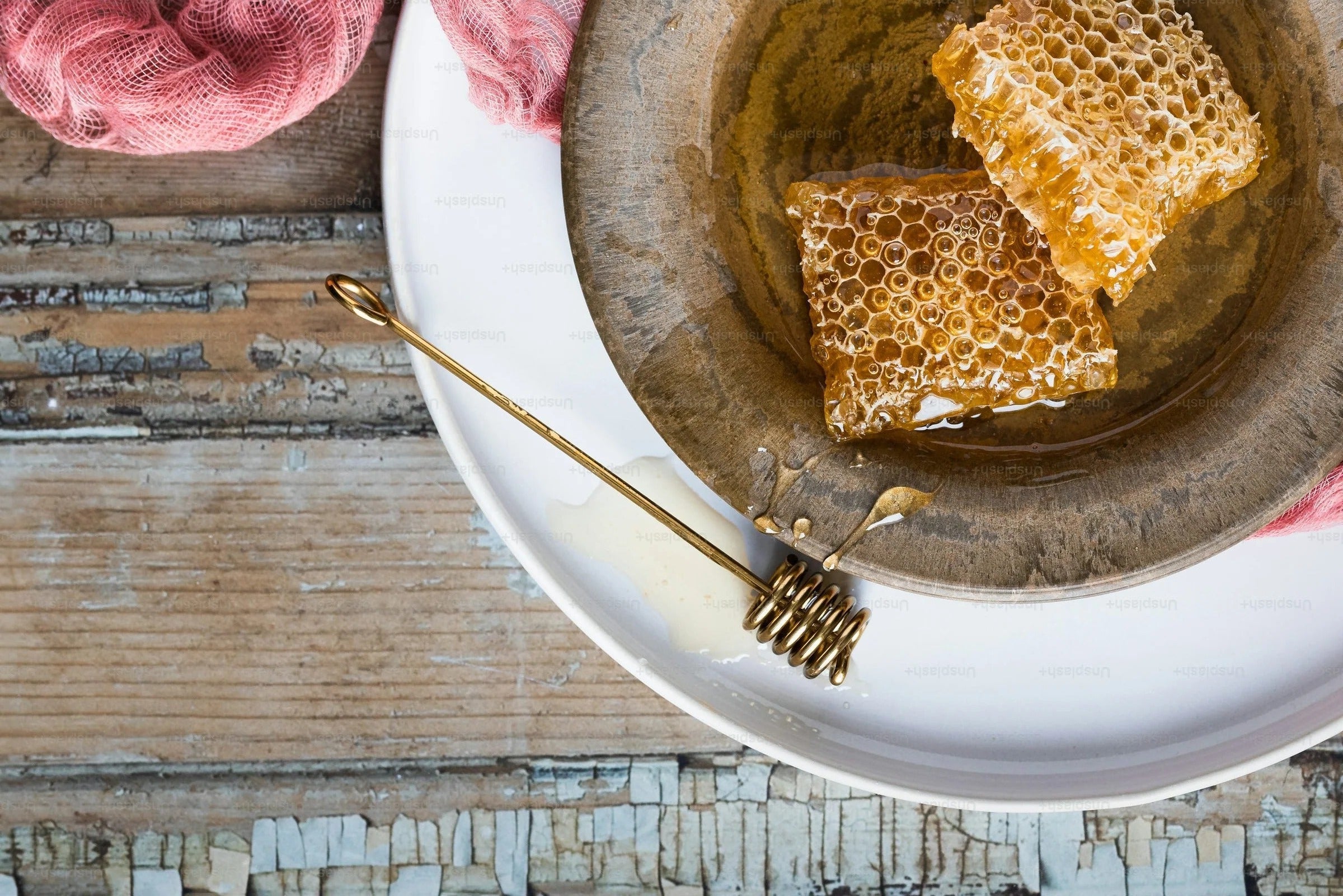 Honeycomb pieces in a bowl with a honey dipper on a rustic wooden surface
